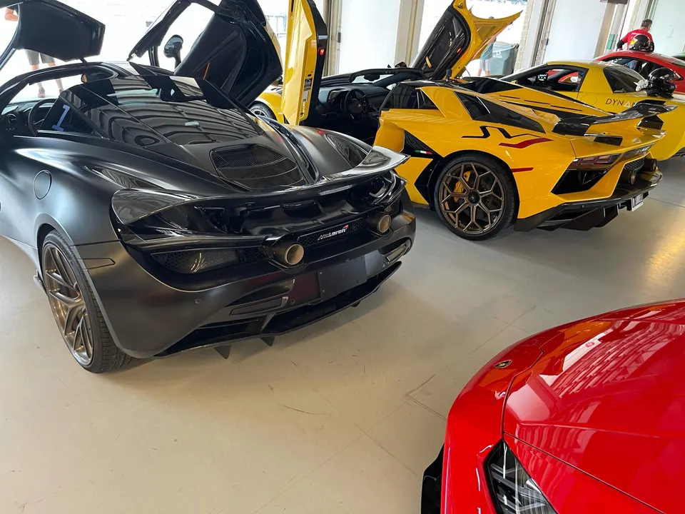 Matte black McLaren 720S, yellow Lamborghini Aventador, and a red Lamborghini parked in a garage with doors open.