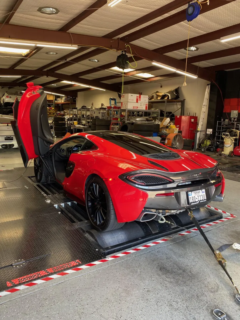 Red McLaren supercar strapped to a dynamometer for performance tuning at a Jotech Motorsports shop
