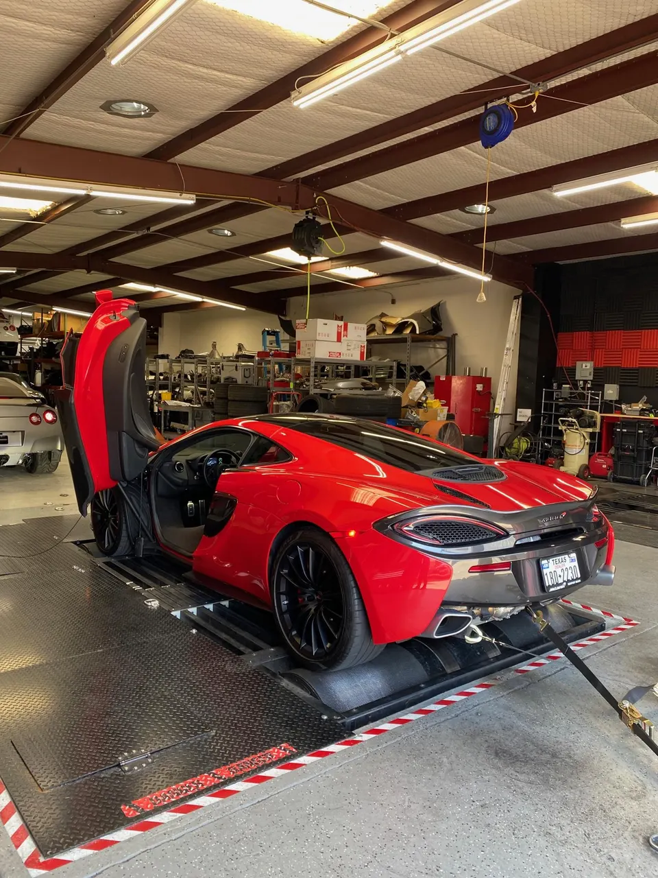 Red McLaren supercar strapped to a dynamometer for performance tuning in a shop setting.