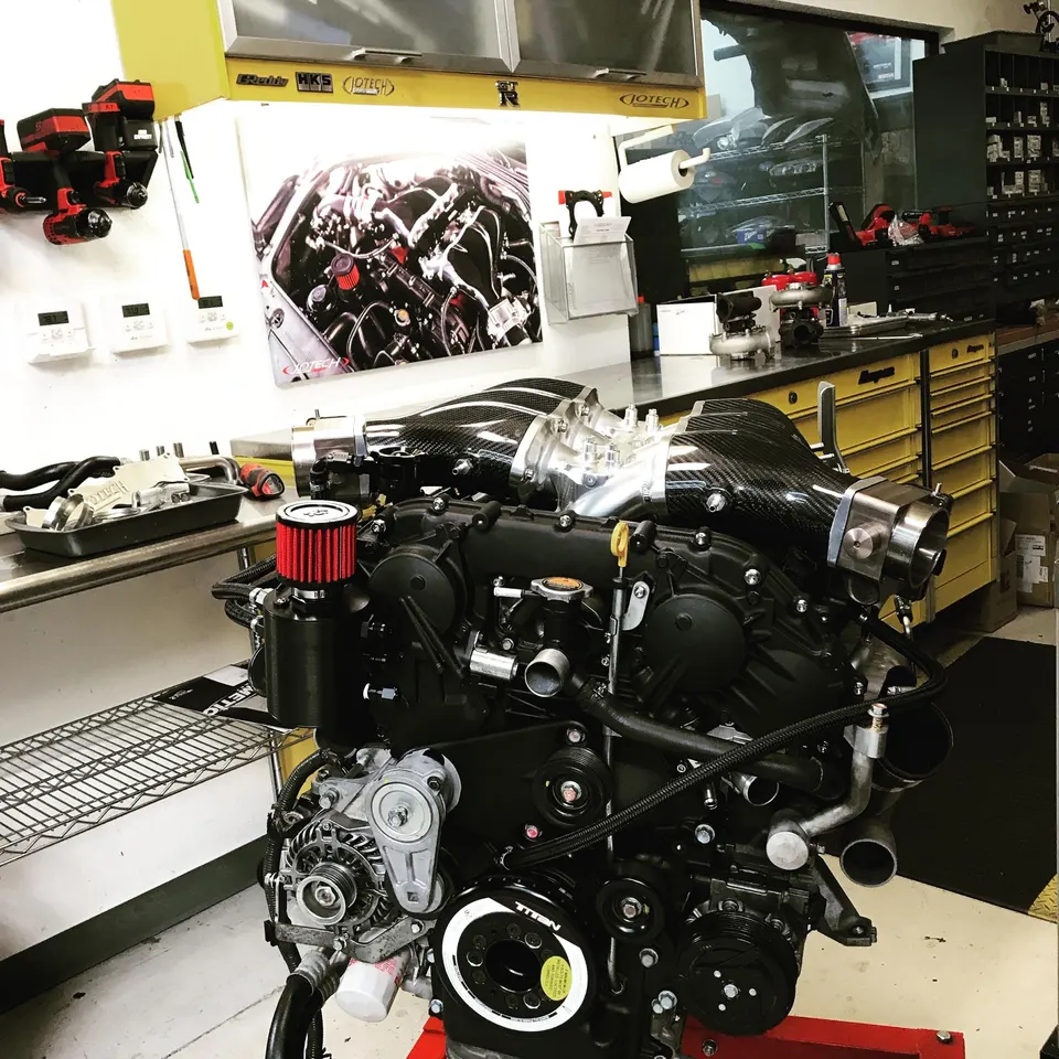 Built engine with carbon fiber intake manifold and red air filter on an engine stand in a performance tuning shop.