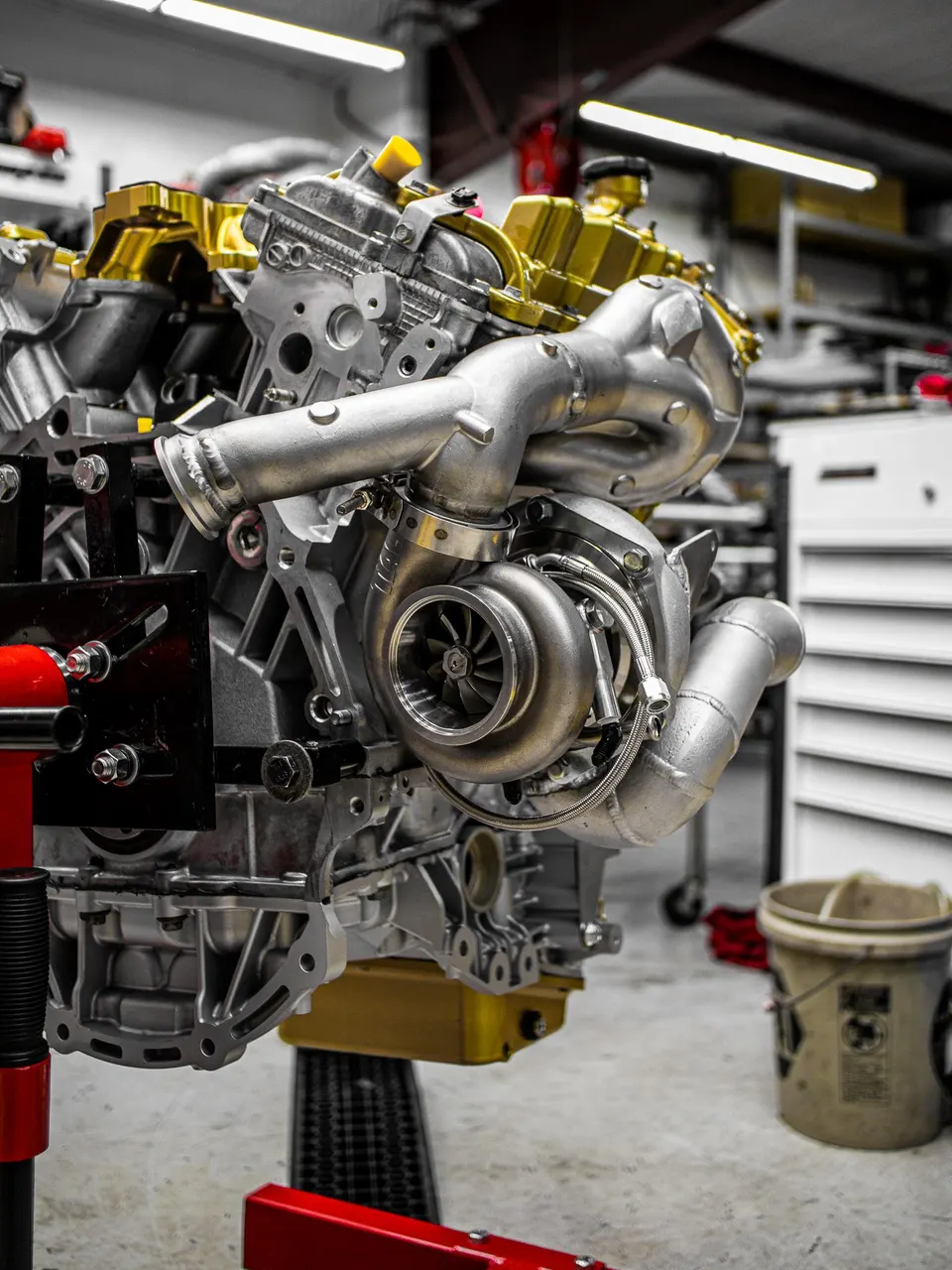 A high-performance engine with a large turbocharger mounted, displayed on an engine stand in a clean workshop environment.