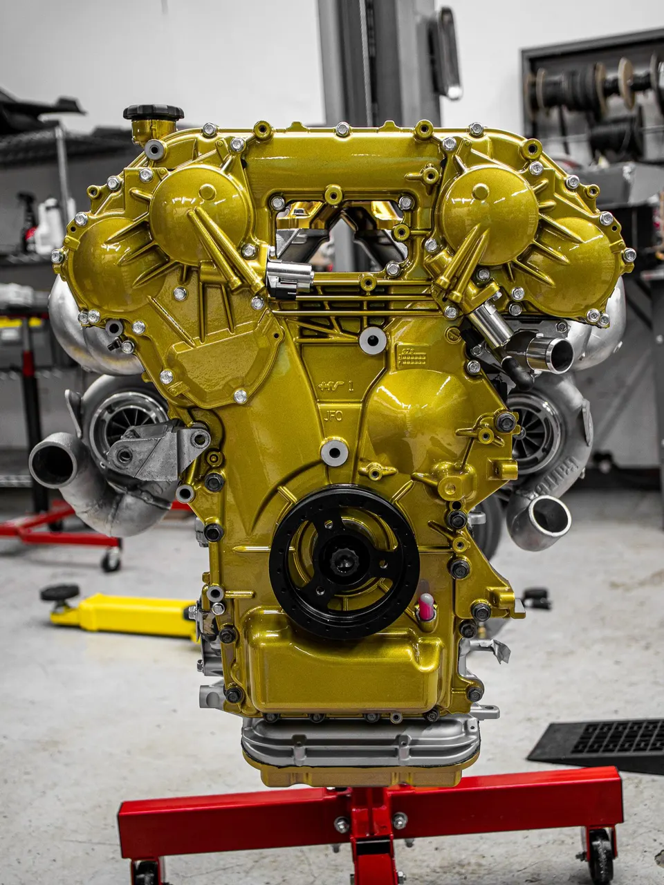 Custom gold built twin-turbo engine on an engine stand in a performance tuning shop.