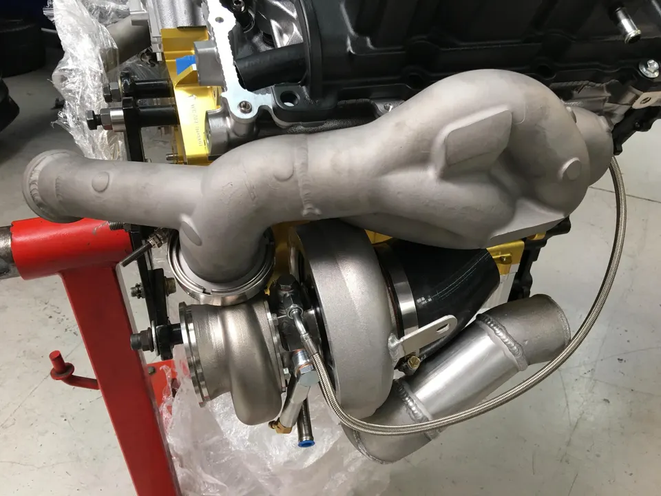 Close-up of a performance engine on an engine stand with a large turbocharger and custom boost piping being installed.