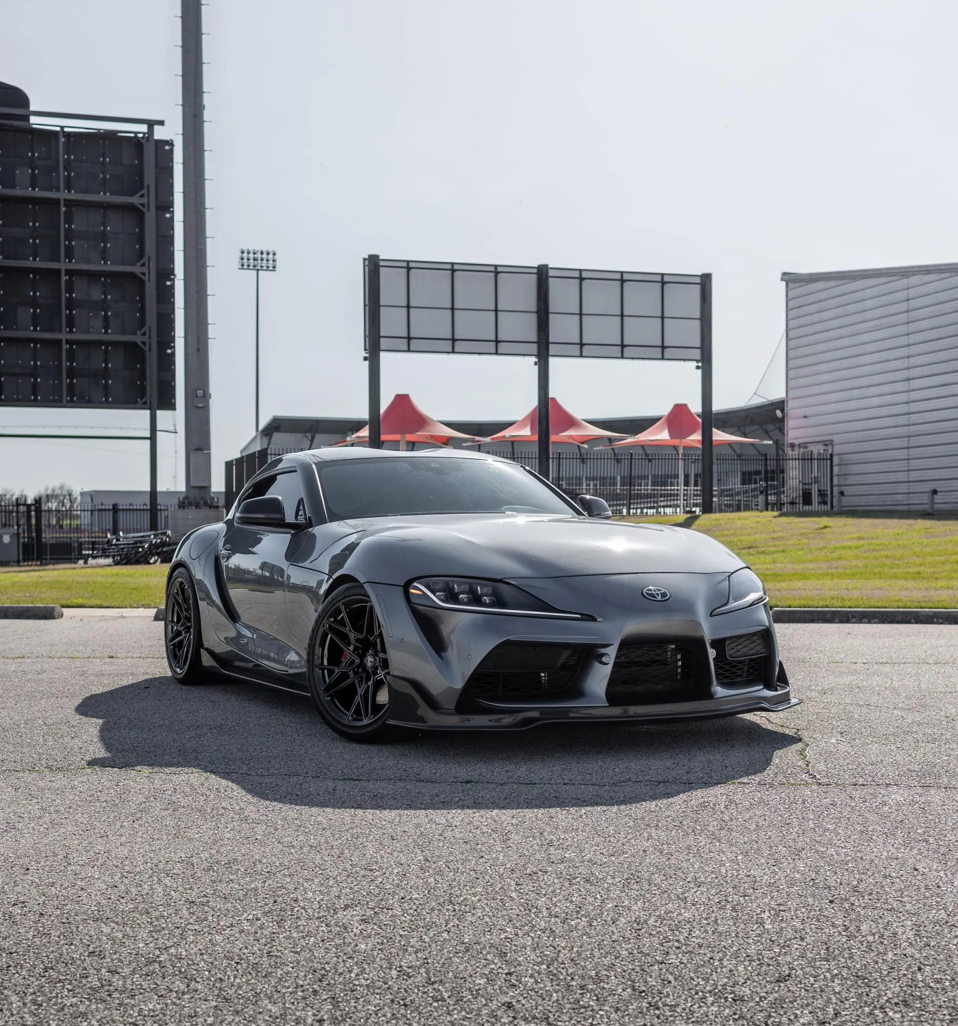 Grey Toyota Supra A90 with aftermarket wheels and a front lip parked outdoors at a venue.