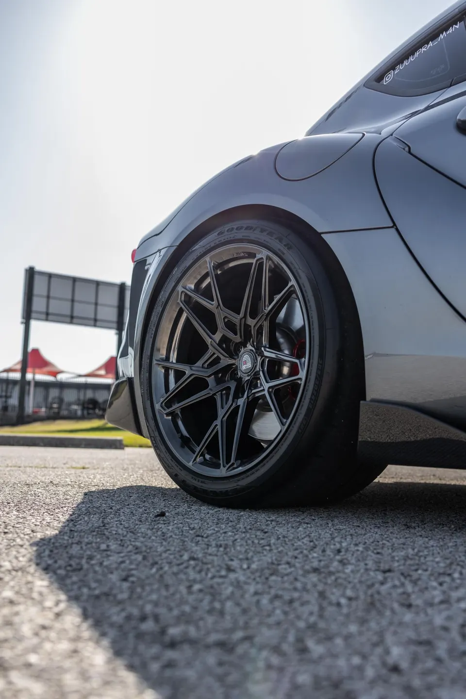 A close-up of a black custom wheel with Goodyear tires and red brake calipers on a grey Toyota Supra.