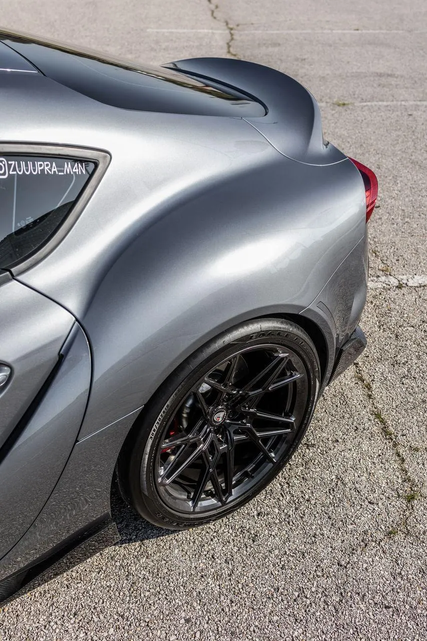 Grey Toyota Supra A90 rear quarter view showcasing aftermarket black multi-spoke wheels and red brake calipers.