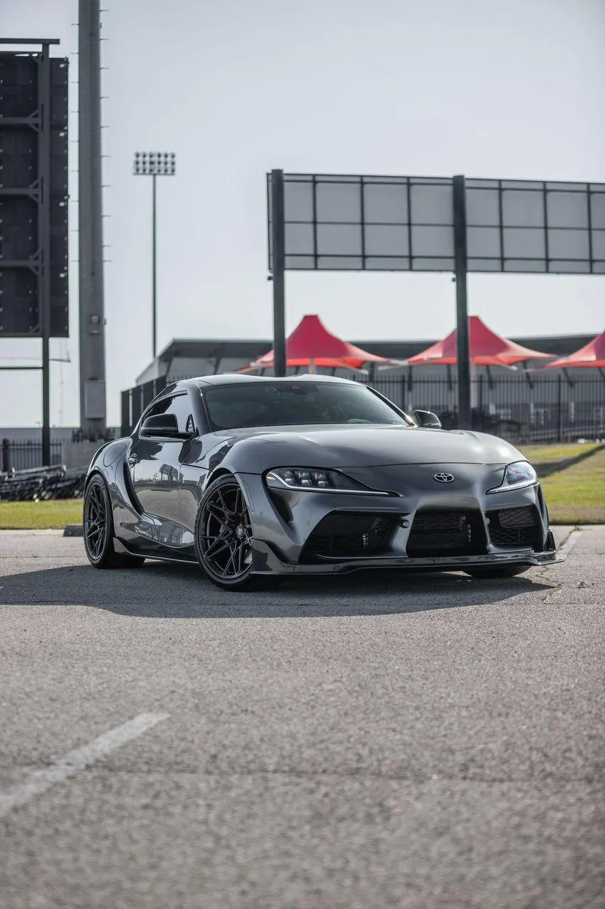 Grey Toyota GR Supra with aftermarket wheels and front splitter parked at a track venue.