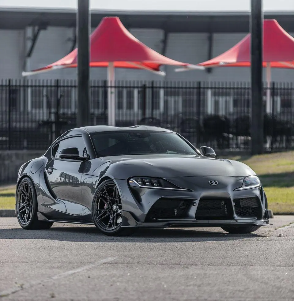 Dark grey Toyota Supra A90 with aftermarket multi-spoke wheels parked outdoors.