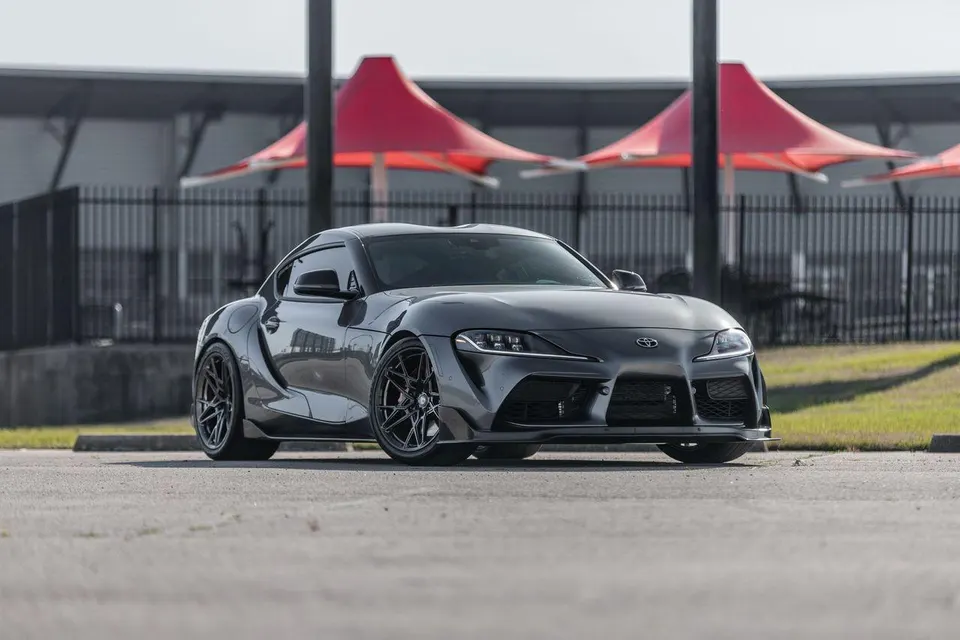 A sleek grey Toyota Supra A90 with aftermarket wheels parked outdoors, showcasing its modified exterior.