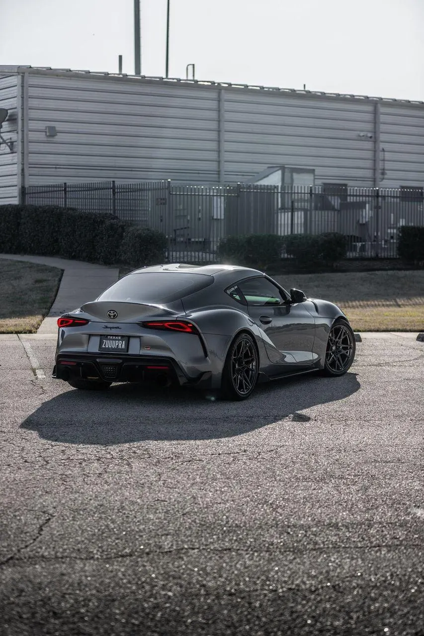 Rear three-quarter view of a grey Toyota GR Supra with aftermarket wheels parked outdoors.