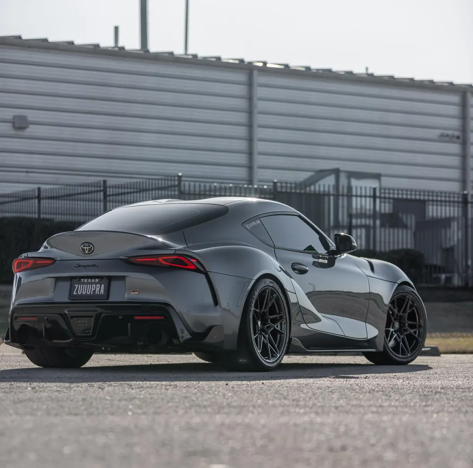 Grey Toyota GR Supra with aftermarket black multi-spoke wheels and custom license plate, parked outdoors.