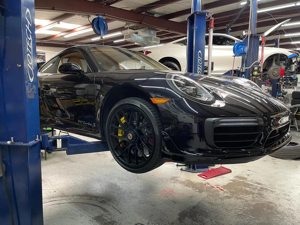 Black Porsche 911 Turbo S on a lift in the Jotech Motorsports shop, ready for service or performance upgrades.