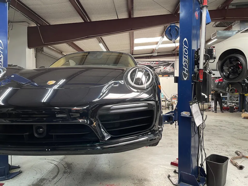 Black Porsche 911 on a car lift in a performance tuning shop, ready for service or modifications.