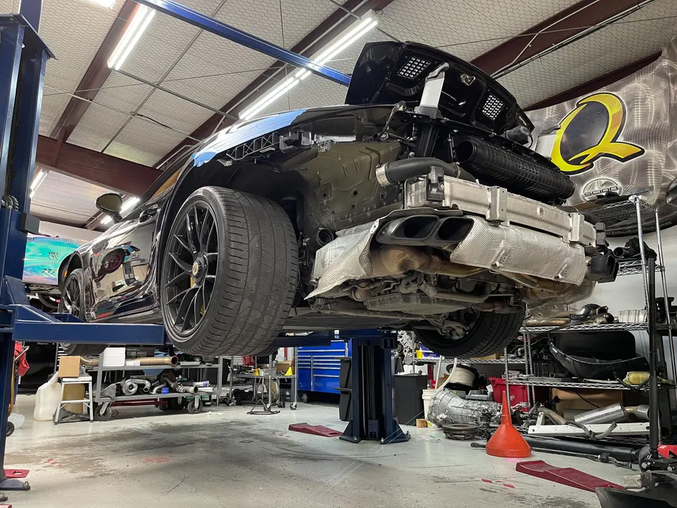 A black Porsche 911 on a car lift in a performance shop, with its rear bumper removed to reveal the exhaust system.