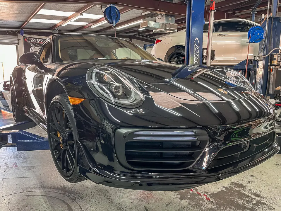 A black Porsche 911 Turbo on a hydraulic lift in a Jotech Motorsports service bay, ready for maintenance or performance upgrades.