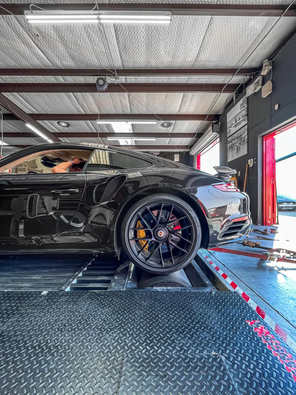 Black Porsche 911 Turbo S on a dynamometer at a performance tuning shop, ready for a dyno run.