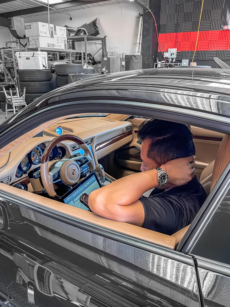 A person tuning a Porsche's electronics with a laptop inside a performance shop.