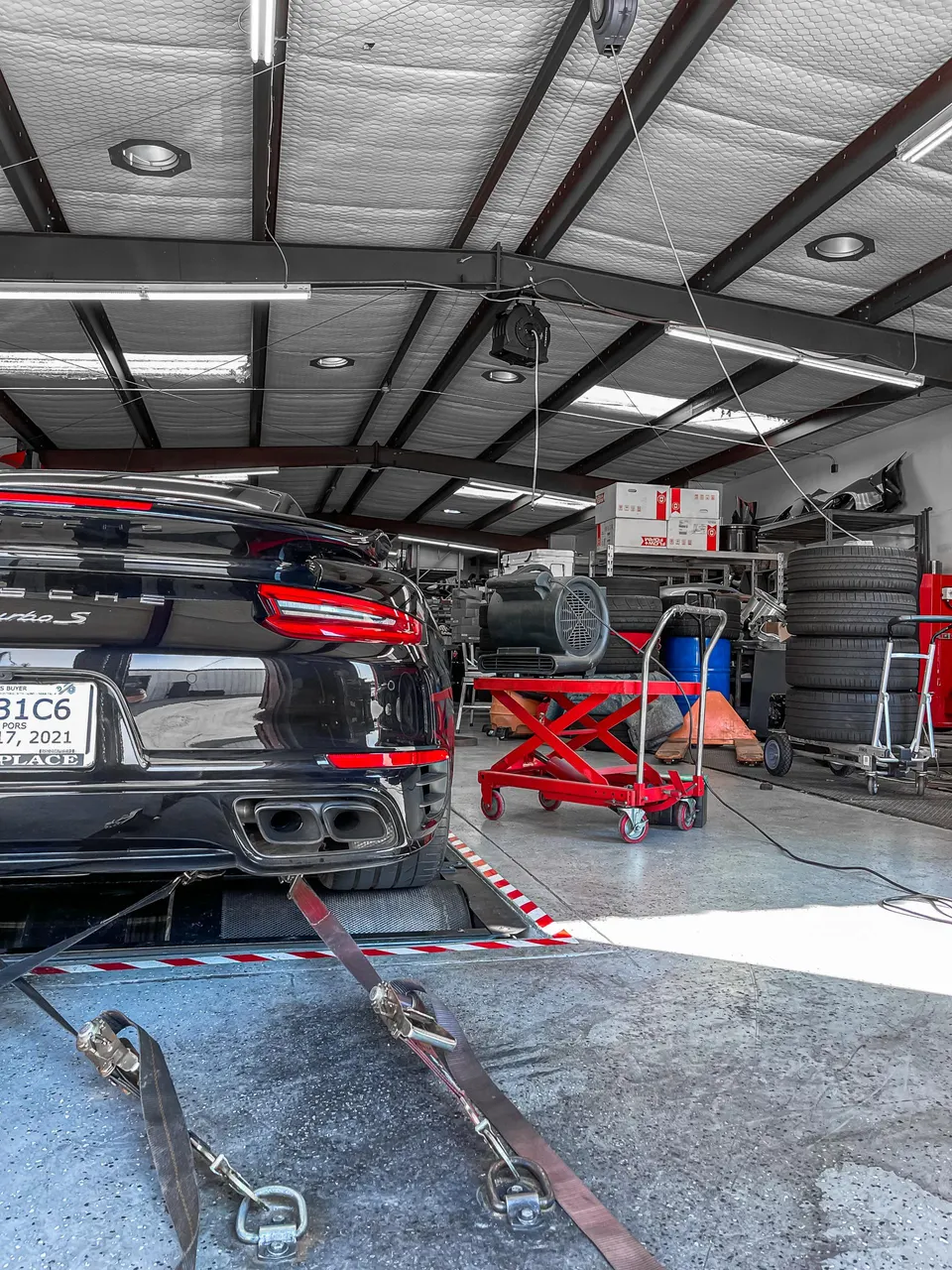 A black Porsche 911 Turbo S on a dynamometer in a performance tuning shop, strapped down for a power run.
