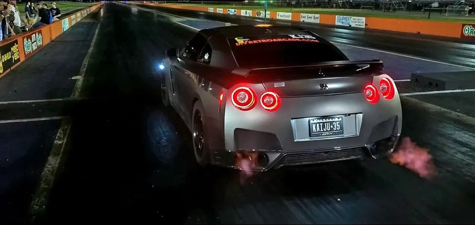 Nissan GT-R R35 on a drag strip at night, launching with flames from the exhaust.