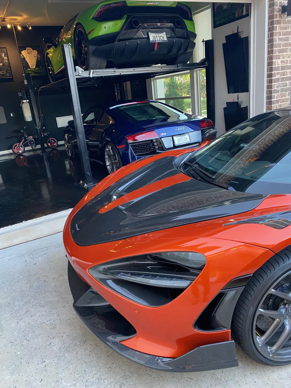 A collection of supercars including an orange McLaren 720S, a green Lamborghini Huracan, and a blue Audi R8 in a garage.