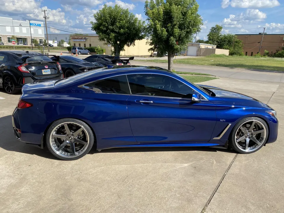 A blue Infiniti Q60 coupe with aftermarket wheels parked outdoors on a sunny day.