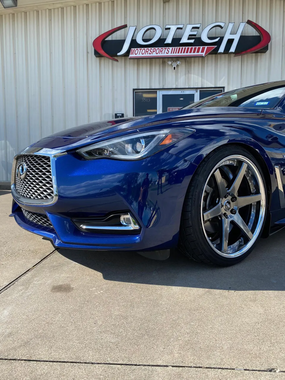 A blue Infiniti Q60 with aftermarket wheels parked outside Jotech Motorsports shop.