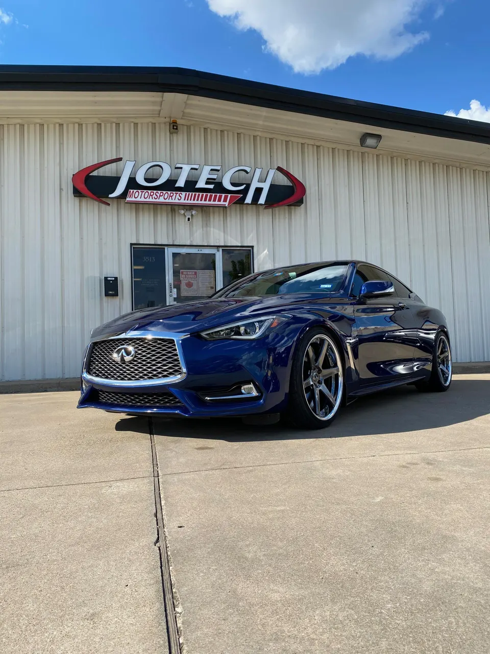 Blue Infiniti Q60 coupe with aftermarket wheels parked outside Jotech Motorsports performance tuning shop.