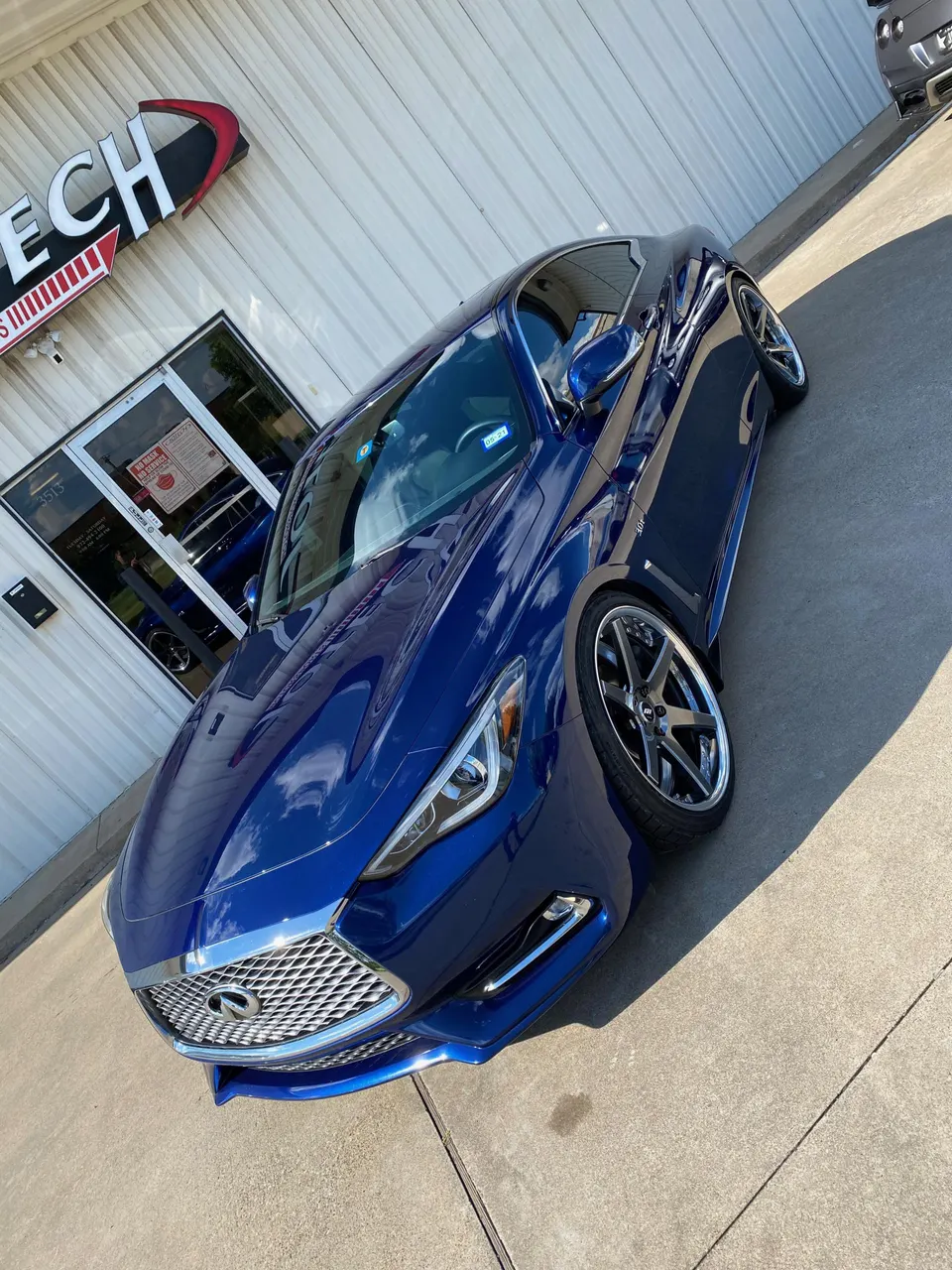 A blue Infiniti Q60 with custom wheels parked outside Jotech Motorsports performance shop.