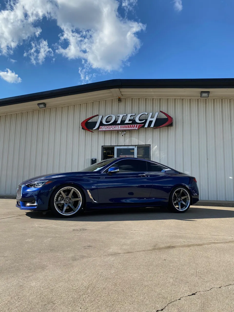Blue Infiniti Q60 coupe with custom wheels parked in front of Jotech Motorsports performance shop.