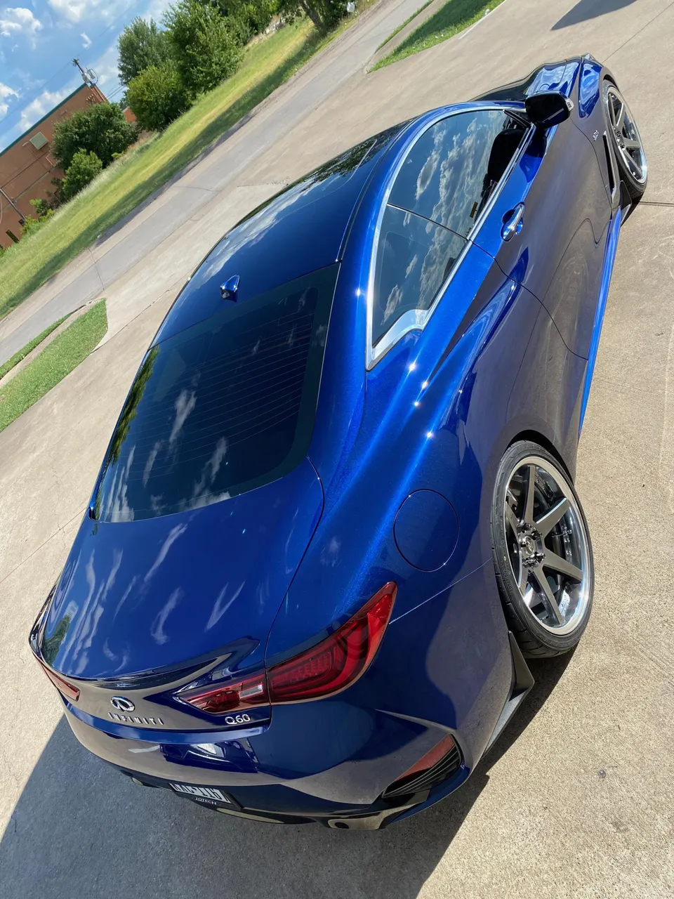 Rear three-quarter view of a shiny blue Infiniti Q60 coupe with custom wheels parked on concrete.