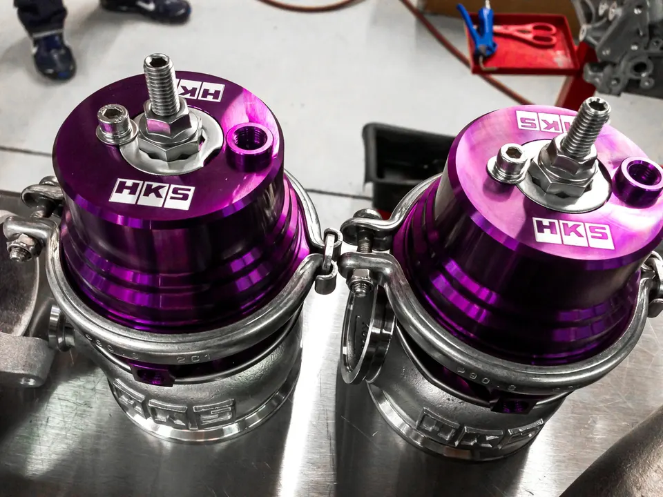 Two purple HKS wastegates on a workbench, ready for installation in a high-performance build.