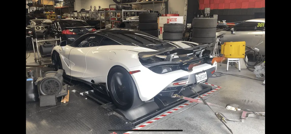 A white McLaren 720S strapped to a dynamometer for performance tuning at a Jotech Motorsports shop.