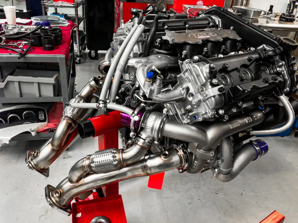 Detailed view of a high-performance engine with twin turbochargers and custom exhaust manifolds on an engine stand in a shop.