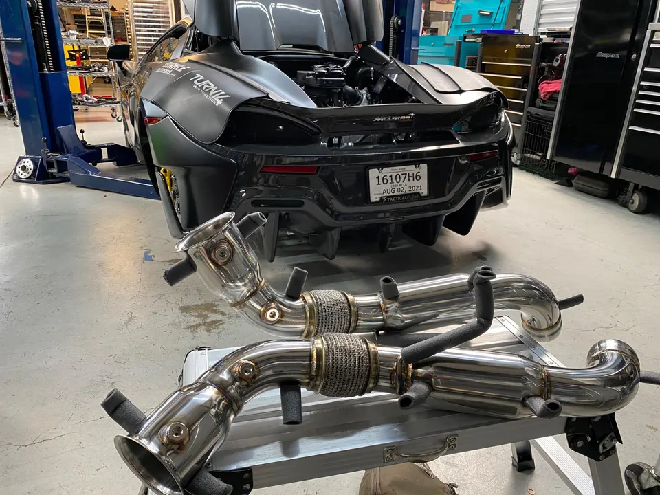 McLaren supercar in a performance shop with new aftermarket exhaust downpipes on a stand, ready for installation.