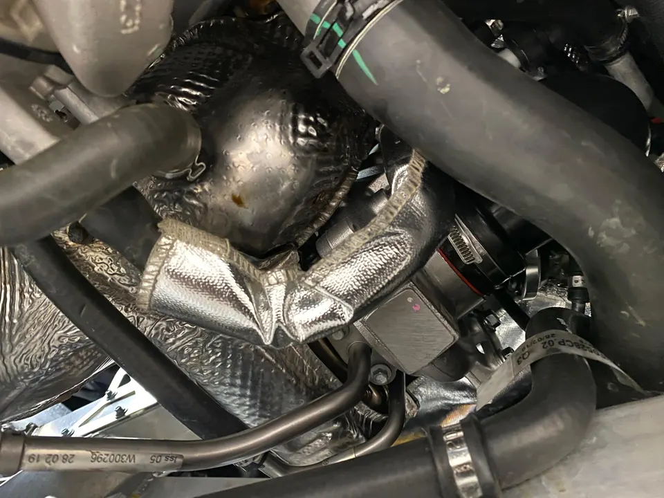 Close-up of an engine bay showing heat shielding, hoses, and various performance components around the turbo area.