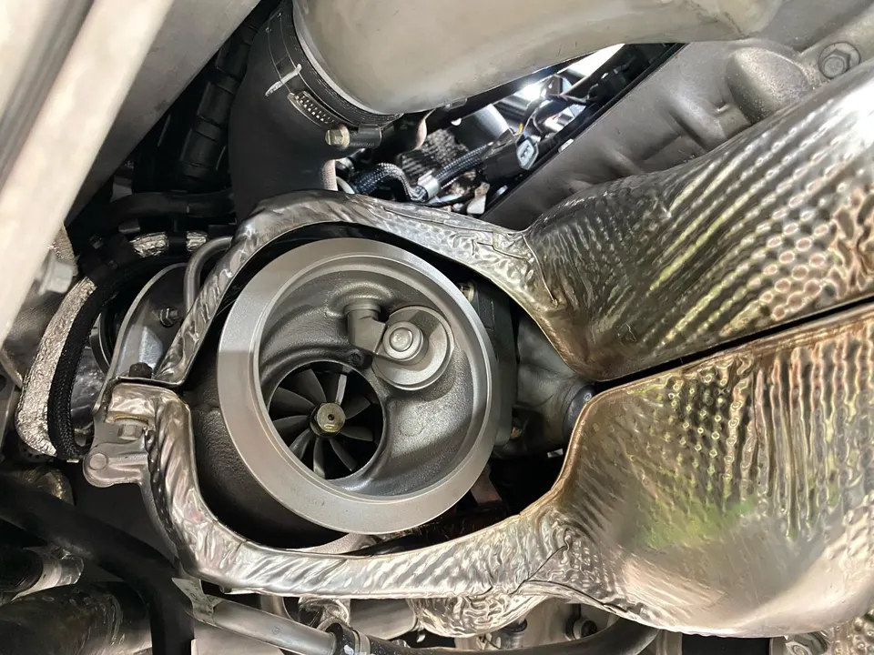 A close-up view of a turbocharger with its compressor wheel and heat shielding in an engine bay.