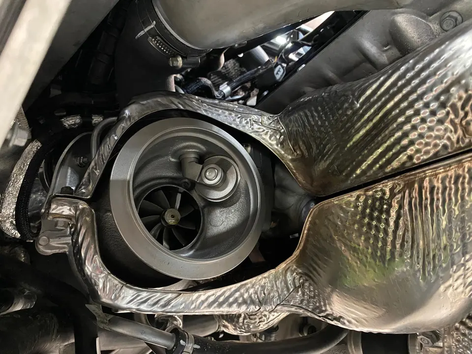 Close-up view of a turbocharger's compressor wheel and surrounding heat shielding in an engine bay.