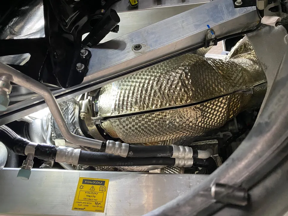 Close-up view of a McLaren engine bay showing a heat-shielded turbocharger and various hoses and lines.