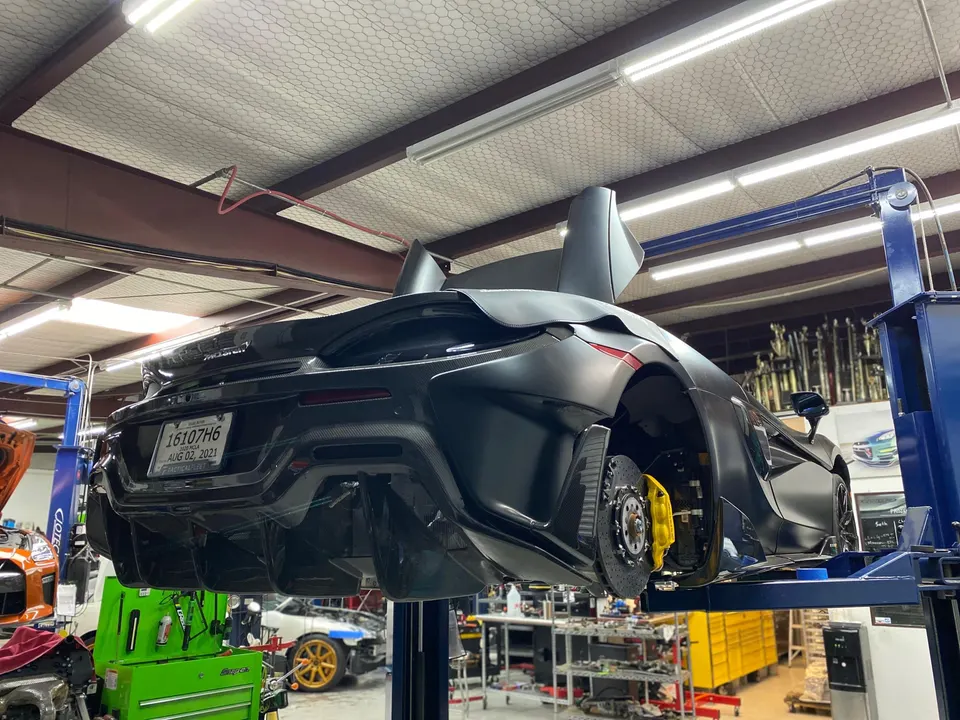 A black McLaren supercar on a lift in a performance tuning shop, with its rear wheels removed exposing yellow brake calipers.