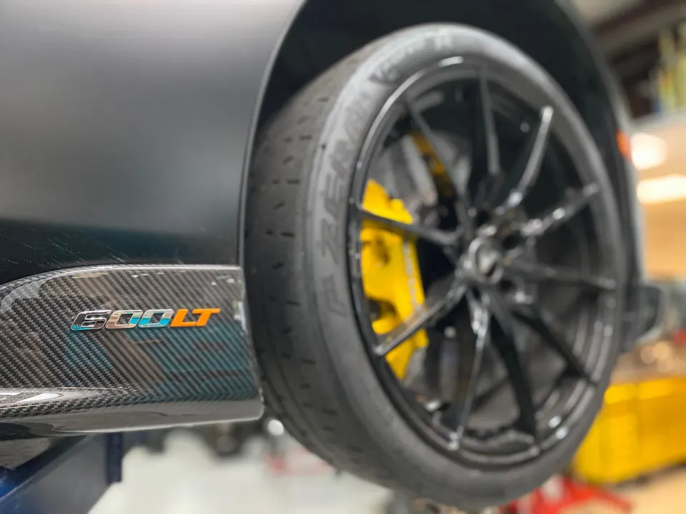 Close-up of a McLaren 600LT on a shop lift, showcasing black wheels, yellow brake calipers, and a carbon fiber side skirt.