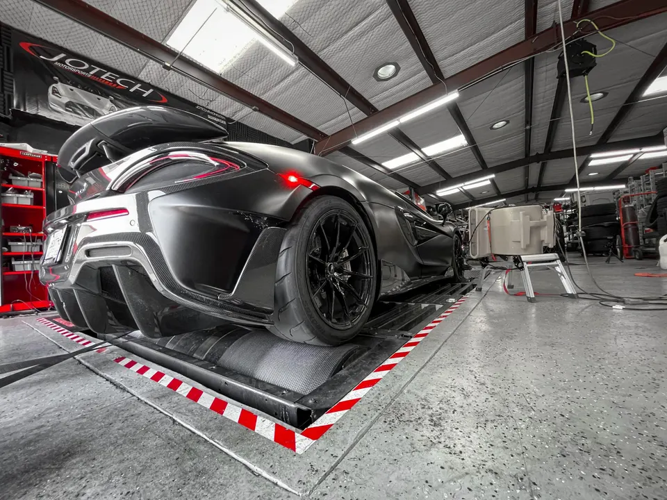 Matte black McLaren supercar on a dynamometer at Jotech Motorsports performance tuning shop.