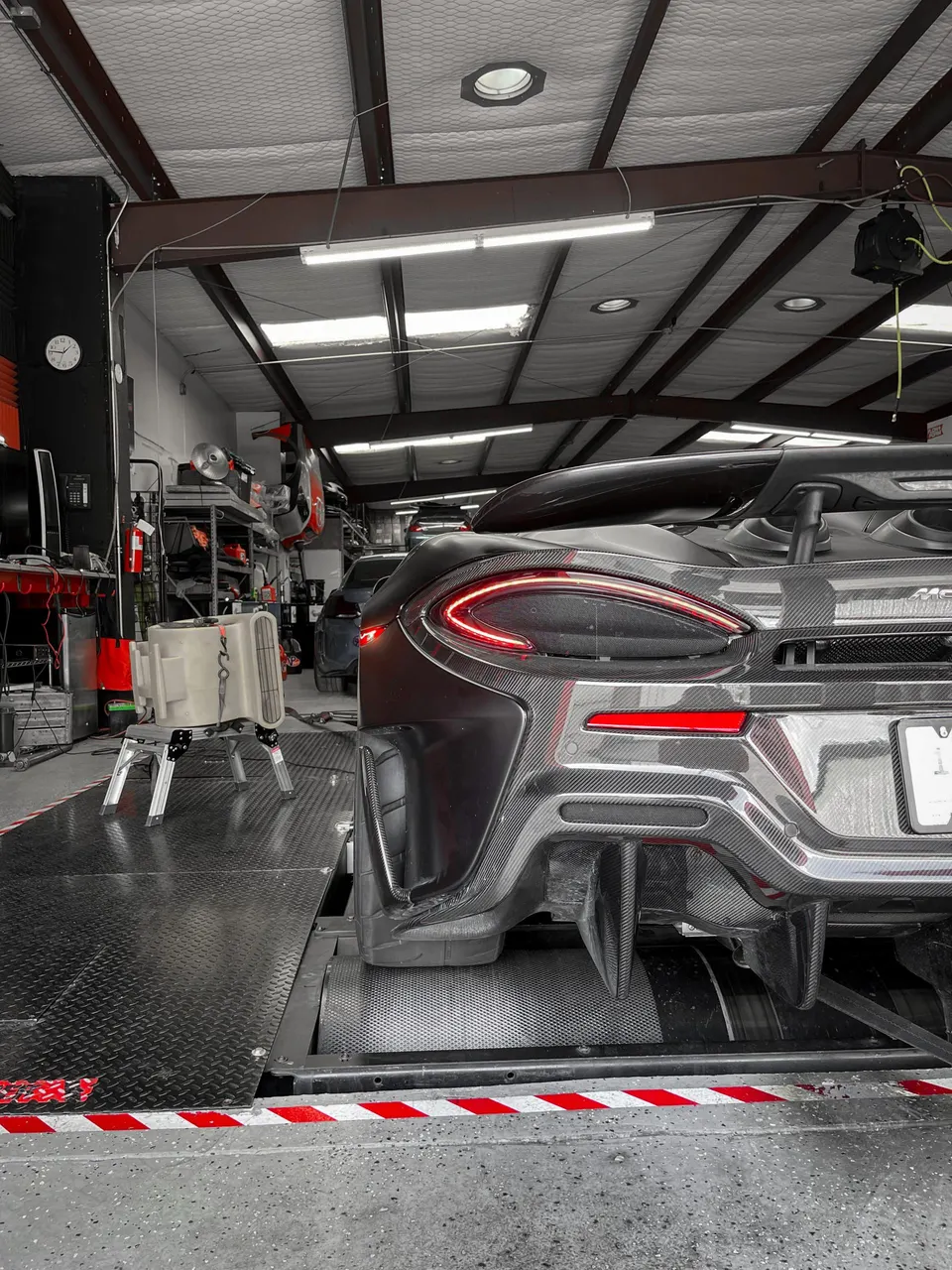 Rear view of a McLaren supercar with a carbon fiber diffuser on a dynamometer at a performance tuning shop.