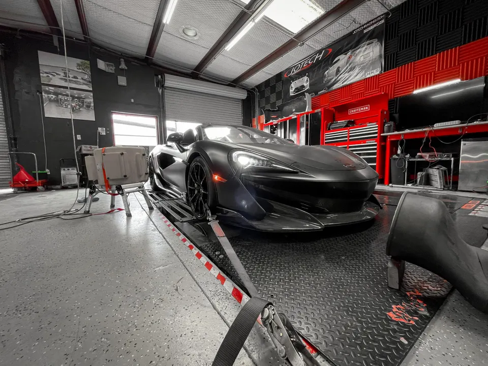 A matte black McLaren 570S strapped to a dynamometer at Jotech Motorsports for performance tuning in a garage.