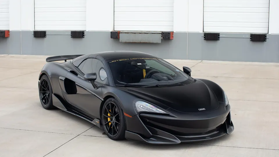 Matte black McLaren 570S with aftermarket aero and yellow brake calipers parked in front of a loading dock.