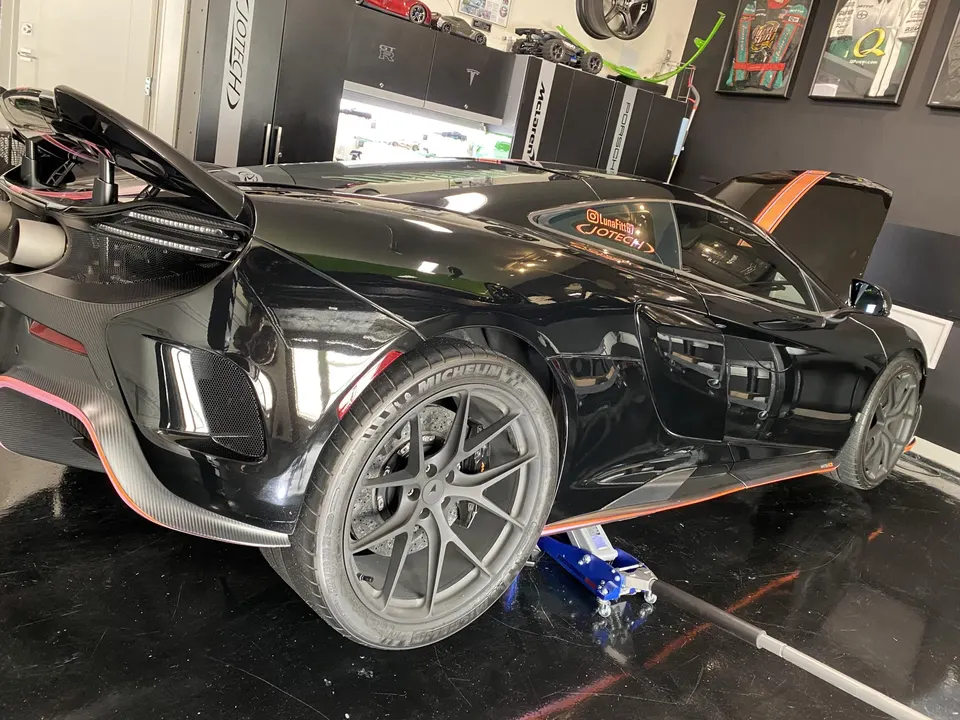 Black McLaren supercar with carbon fiber aero and aftermarket wheels lifted on a jack in a Jotech Motorsports shop.