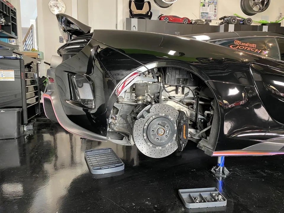 Black McLaren supercar in a shop with the rear wheel removed, showcasing the carbon ceramic brakes and suspension.
