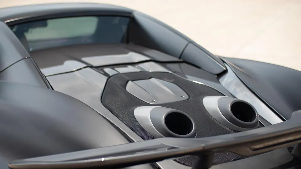 A close-up of the rear of a matte grey McLaren supercar, showcasing the dual exhaust tips and carbon fiber rear wing.