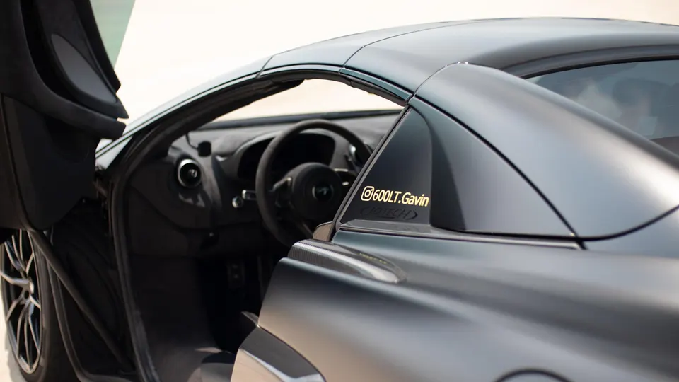 A close-up of a gray McLaren 600LT's side profile with the driver's door open, revealing the interior and steering wheel.