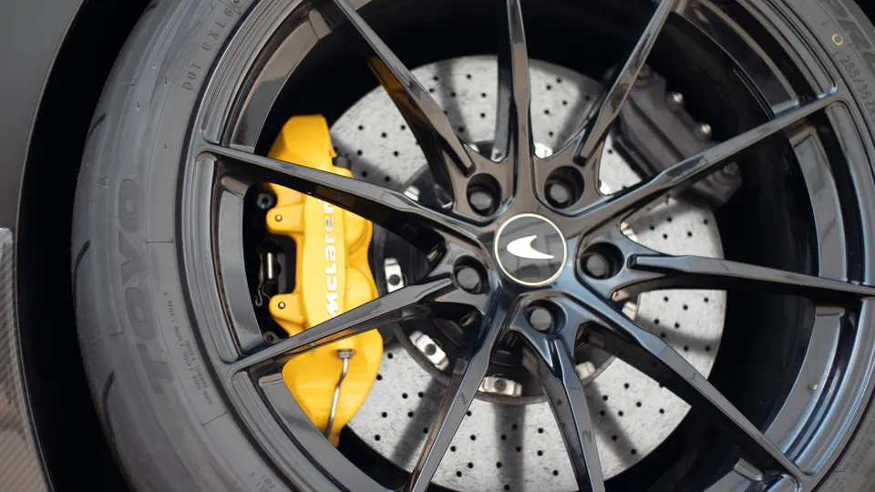 A close-up of a McLaren's black multi-spoke wheel, yellow brake caliper, and Toyo tire.