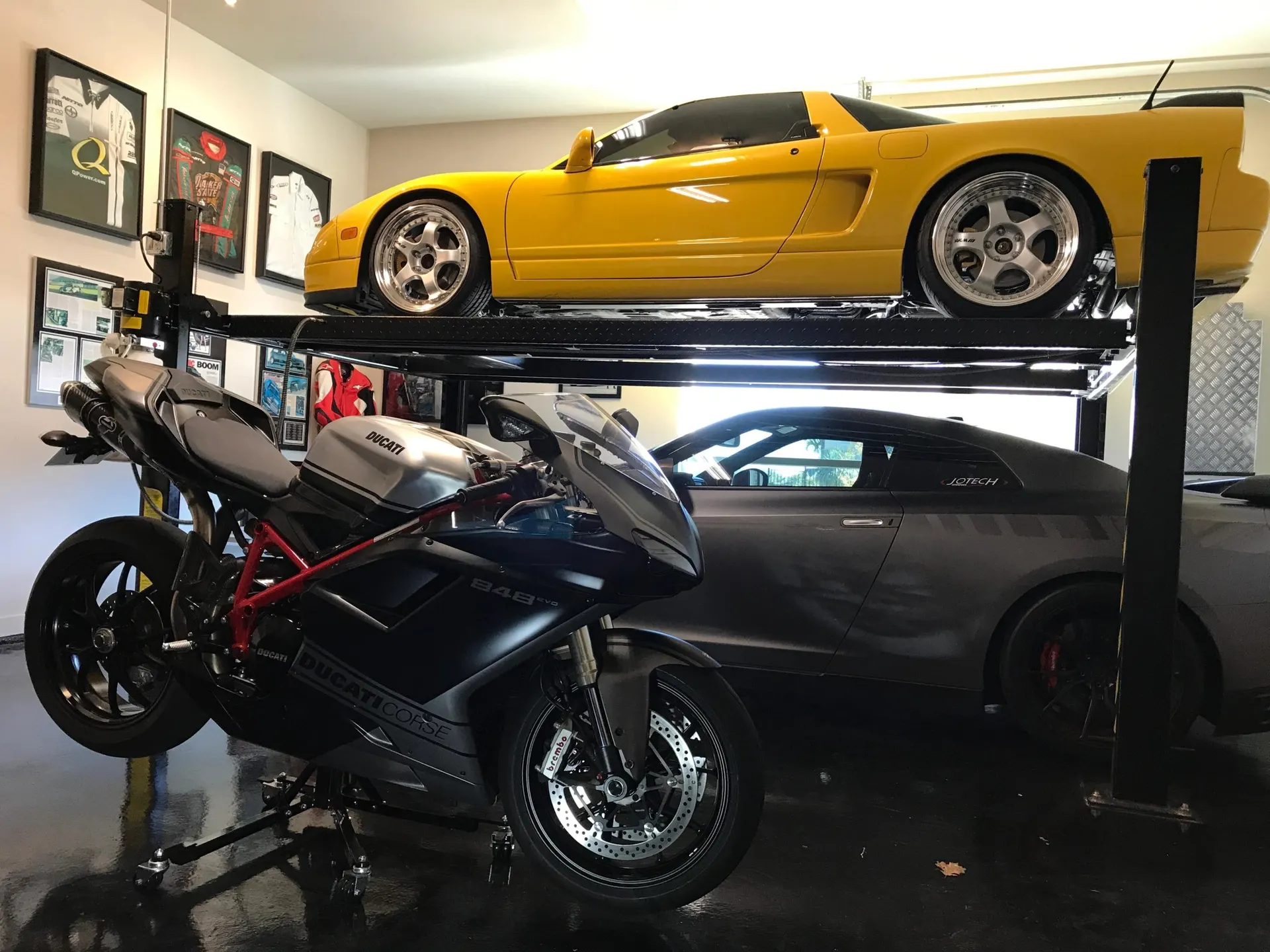 Yellow Honda NSX on a car lift above a grey Nissan GT-R and a black Ducati motorcycle in a clean garage.